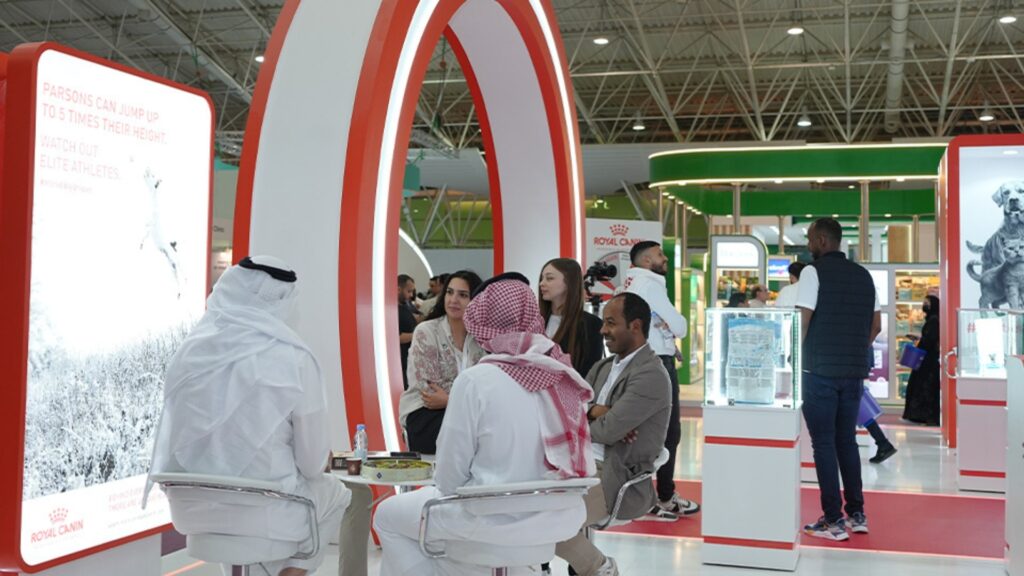 Group of people sitting at a table in front of a white and red circle gateway at an expo,